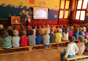 Dzieci ze starszych wraz z prowadząca spotkanie oglądają film edukacyjny na tablicy multimedialnej.